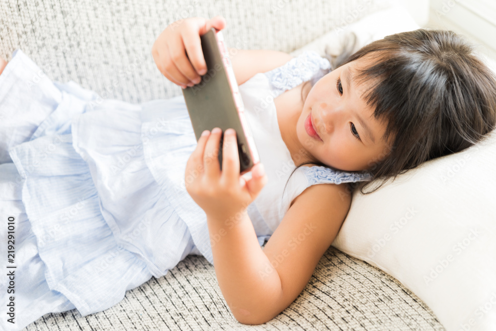 Cute little girl having fun to play game on smart phone lying on sofa. Cute little girl having fun to play game on smart phone lying on sofa.