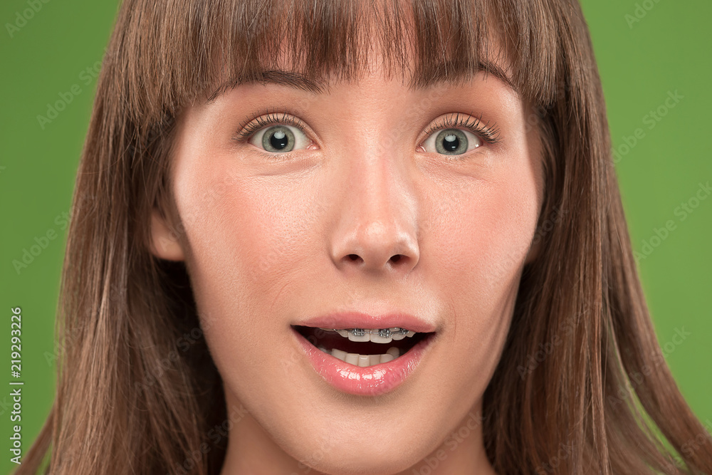 Beautiful young surprised woman with teeth braces on green Beautiful young surprised woman with teeth braces on green