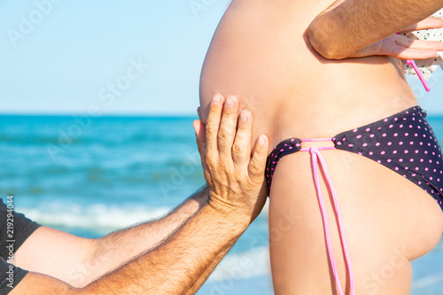 A man is holding a pregnant woman by the stomach on the beach, by the sea. The concept of family, love, new life and peace, the expectation of the child.