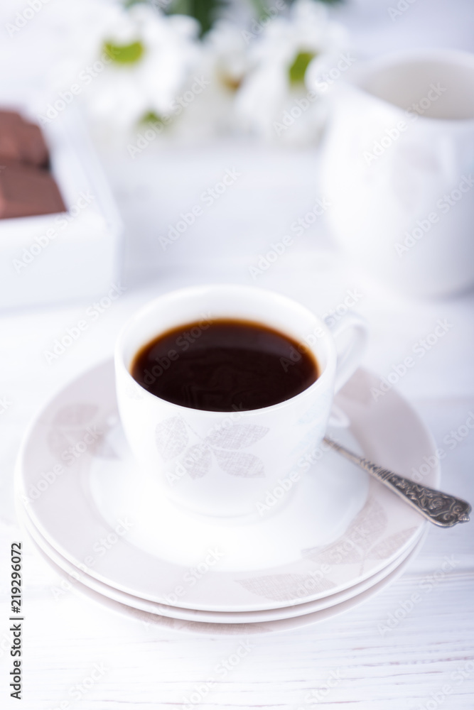 Porcelain cup of black coffee and chrysanthemums flowers on a white background