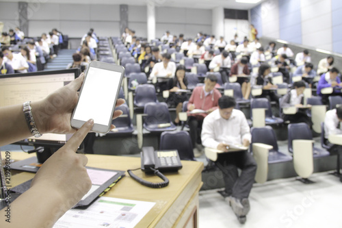 Female using phone in class and blur background of students during study or quiz, test and exams from teacher or in large lecture room / University classroom.