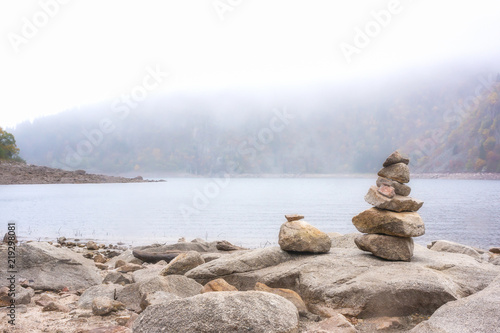 Photography Stack of stones alongside a mountain lake on a misty foggy moody day with copy space, Lac Blanc, Vosges mountains, France