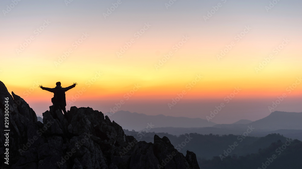 silhouette of a standing man on top of a cliff mountain with arms raised during sunset celebrate success - landscape sunset Thailand
