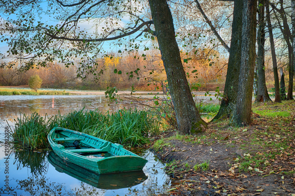 Green abandoned boat in the lake in a beautiful autumn park in the early morning