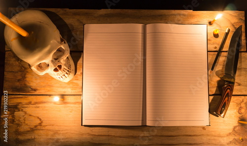 Human skull with candle light and notebook with pencil and knife on wooden table, Decorated for Halloween Theme with copy space.