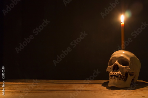 Human skull with candle light on wooden table in the dark background, Decorate for Halloween Theme with copy space.