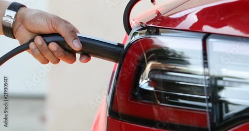 Close up of a red electric car's charge port being opened automatically using a smart phone, and being plugged in.