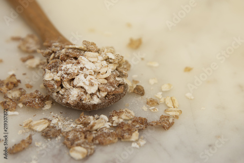 Oat flakes in wooden spoon over marbble background, healthy cereal ingredient.