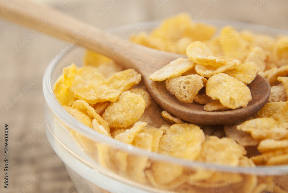 bowl of sugar-coated corn flakes and spoon for breakfast or snack over rustic wooden background. bowl of sugar-coated corn flakes and spoon for breakfast or snack over rustic wooden background.