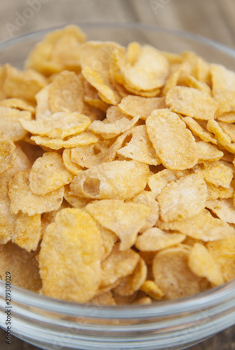 bowl of sugar-coated corn flakes and spoon for breakfast or snack over rustic wooden background.