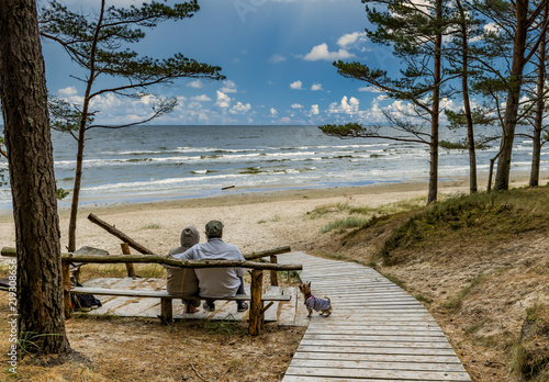 Happy couples of seniors are resting and looking at a distance near a sandy b...