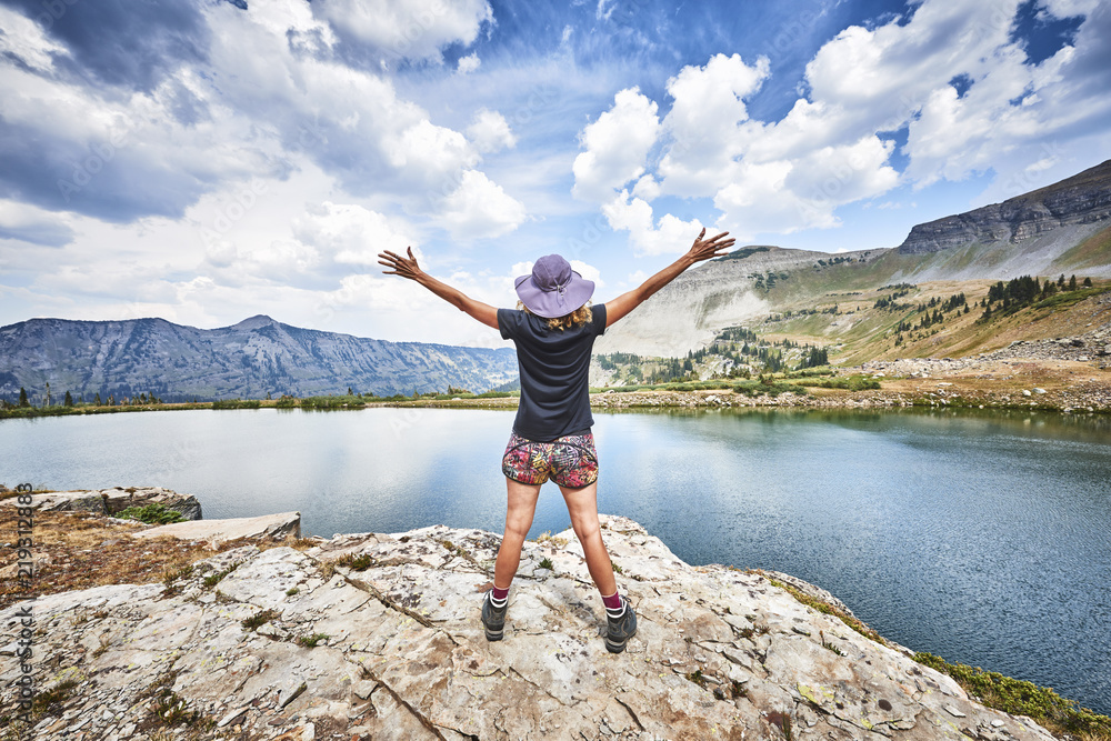 Obraz premium a young woman standing on top of a mountain with arms raised in excitement