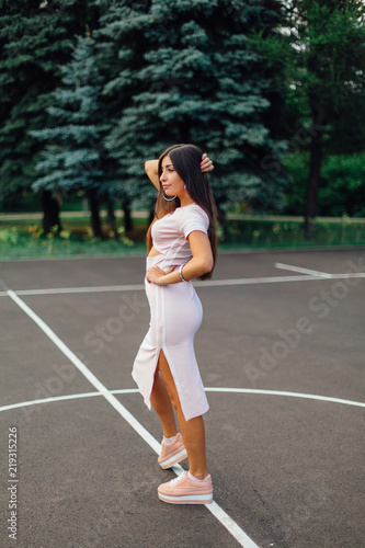 Charming brunette female dressed in a pink dress posing on the basketball court.