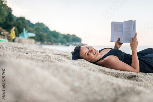 Smiling young woman reading a book on the beach. Copy space.