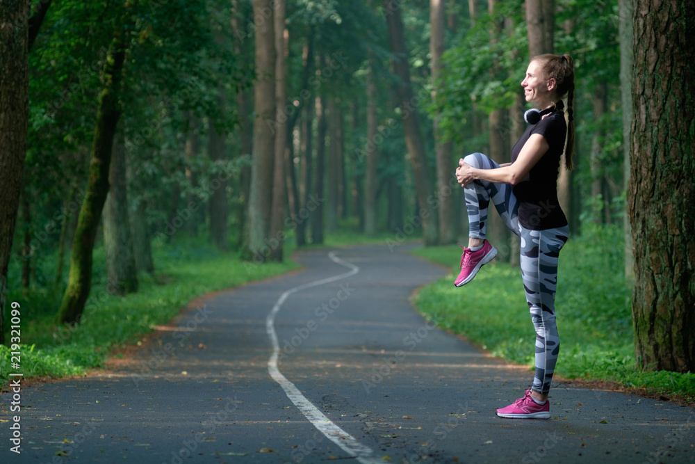 Fototapeta premium Beautiful attractive young woman stretching in the park and listen music