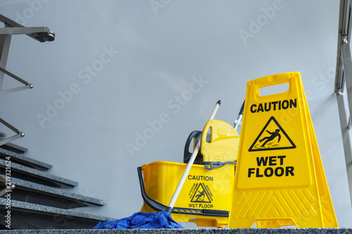 Safety sign with phrase Caution wet floor and mop bucket, indoors. Cleaning service photo