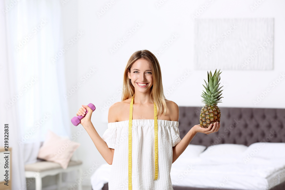 Happy slim woman with measuring tape, dumbbell and pineapple at home. Positive weight loss diet results Happy slim woman with measuring tape, dumbbell and pineapple at home. Positive weight loss diet results