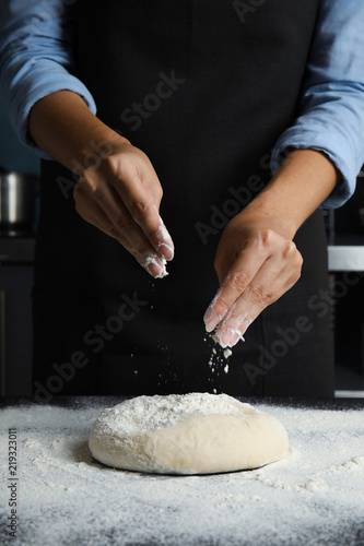 Woman sprinkling dough for pastry with flour on table