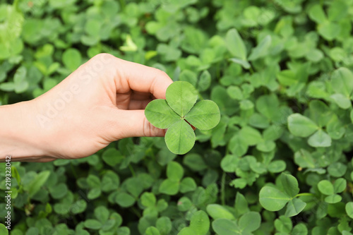 Woman holding four-leaf clover outdoors, closeup