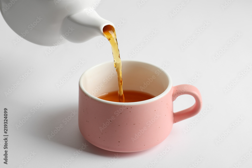 Pouring hot tea into ceramic cup on white background Pouring hot tea into ceramic cup on white background