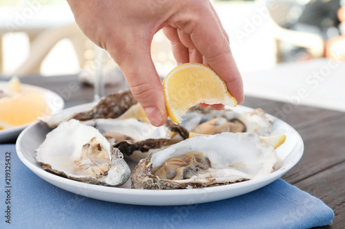 Woman squeezing lemon onto fresh tasty oysters on plate