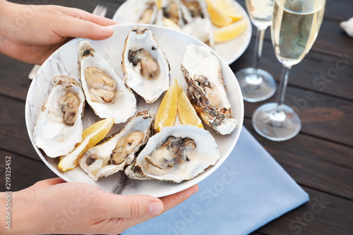 Woman with plate of fresh oysters over table, focus on hands