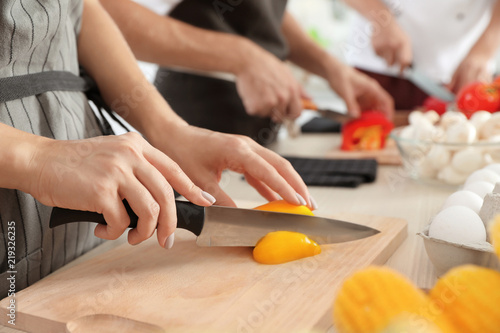 Female chef cutting paprika on wooden board at table, closeup