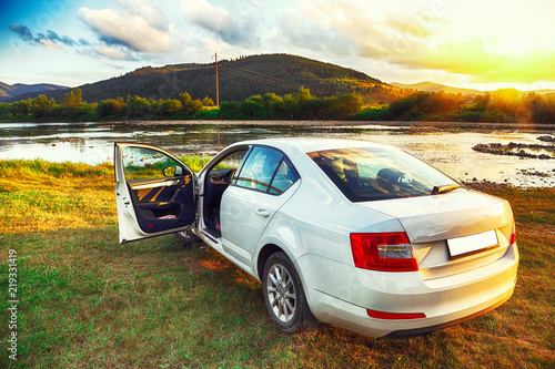 White car in beautiful mountains with scenic view at sunset time near river
