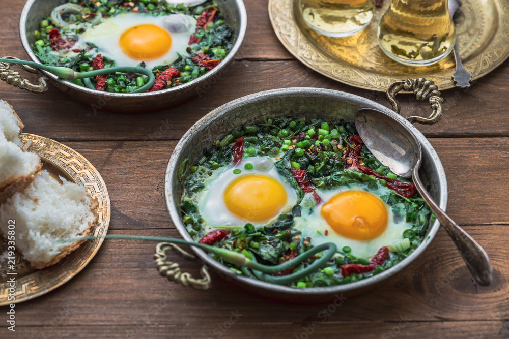 Green shakshuka. Fried eggs with fresh spinach, ramson, leek in a pan on a gray background, top view Green shakshuka. Fried eggs with fresh spinach, ramson, leek in a pan on a gray background, top view