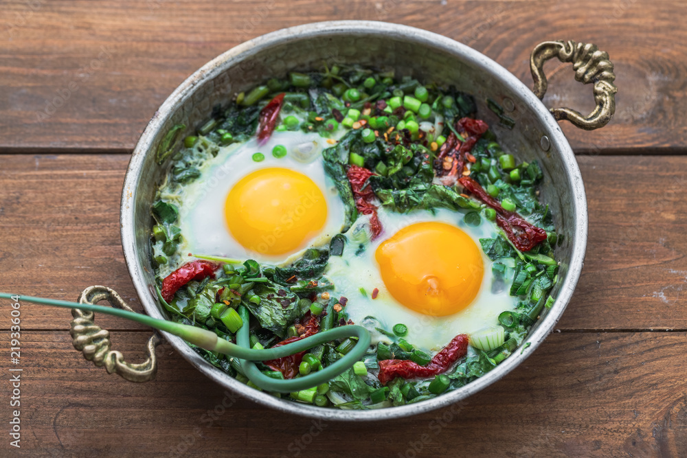 Green shakshuka. Fried eggs with fresh spinach, ramson, leek in a pan on a gray background, top view Green shakshuka. Fried eggs with fresh spinach, ramson, leek in a pan on a gray background, top view