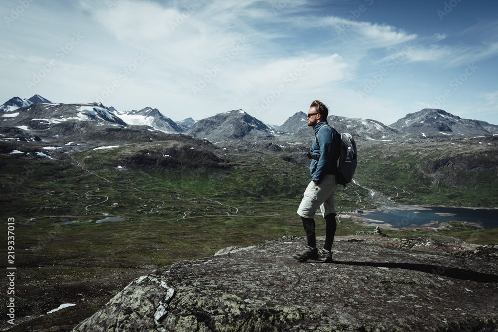 Man hiker with a backpack on the peak top enjoying the view. Concept of a feeling of accomplishment. Hiking in Jotunheimen national park Oppland, Norway. 