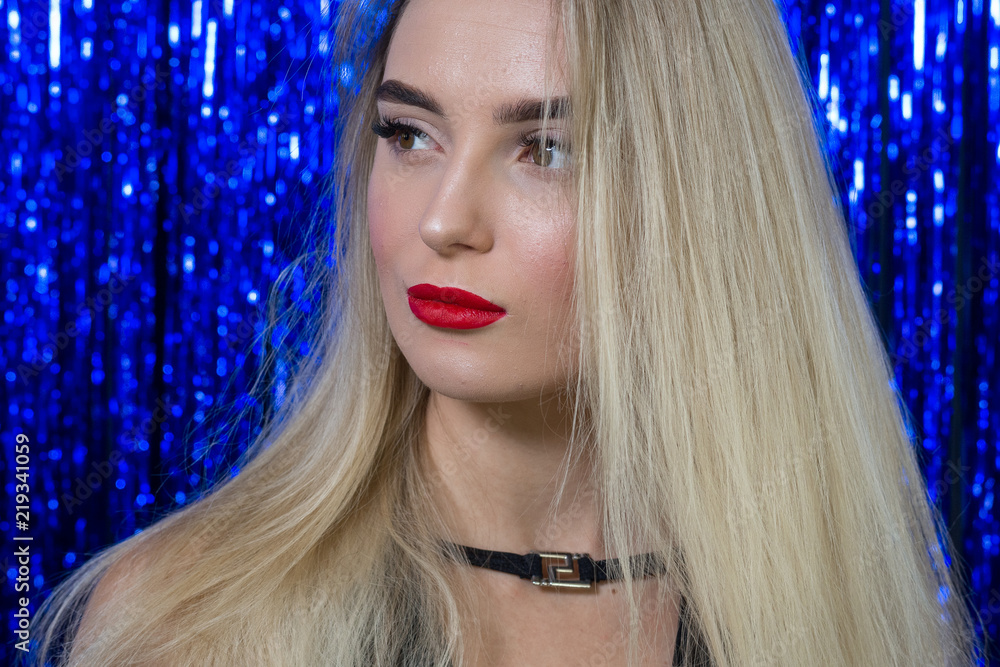sexy blonde girl with red lipstick on lips in black dress posing on camera  against the background of shiny blue pajetoks Stock Photo | Adobe Stock