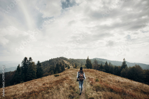 hipster traveler with backpack walking on top of mountains. wanderlust and travel concept with space for text. stylish woman hiking. atmospheric epic moment