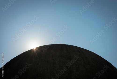 The sun breaking over the edge of a silhouetted dome, appearing like the sun over a distant planet