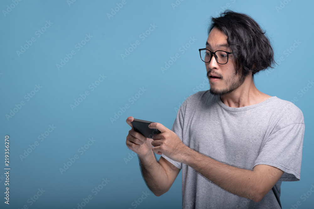 Surprise Young bearded man playing mobile games in blue background. Surprise Young bearded man playing mobile games in blue background.