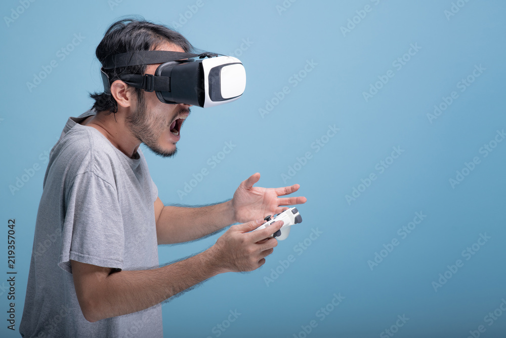 Young bearded man playing VR game in blue background. Young bearded man playing VR game in blue background.