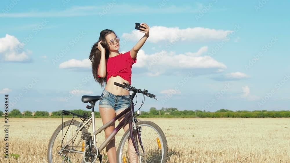 The girl makes selfie. A sporty girl with a bicycle takes a picture of herself on the phone. The girl makes selfie. A sporty girl with a bicycle takes a picture of herself on the phone.