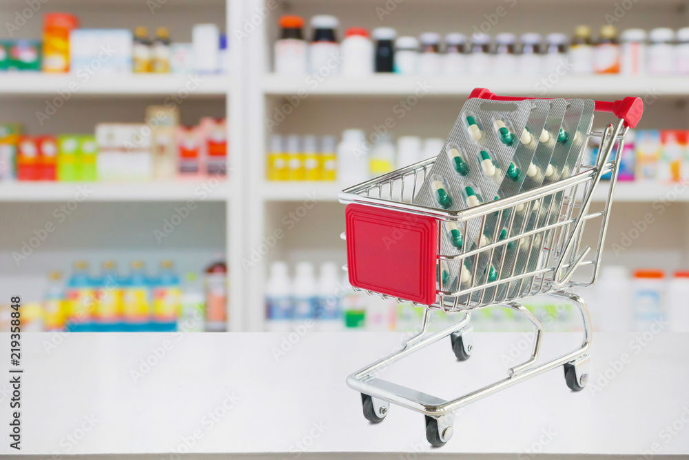 medicine pills capsule in shopping cart on pharmacy store counter with blur drugstore shelves defocused background medicine pills capsule in shopping cart on pharmacy store counter with blur drugstore shelves defocused background