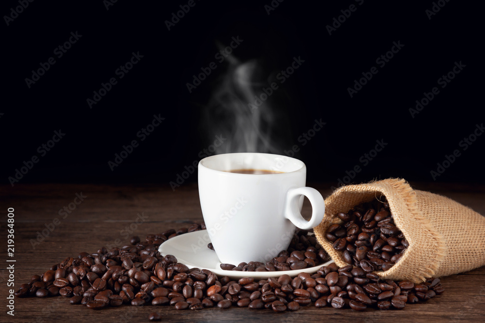 A cup of hot coffee on a wooden table with roasted coffee beans