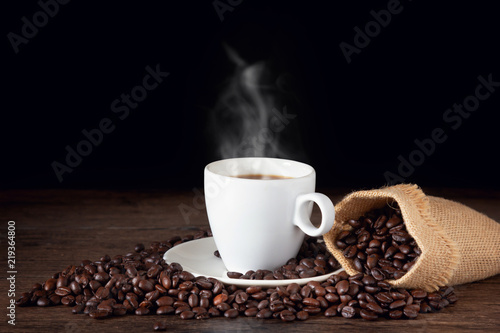 A cup of hot coffee on a wooden table with roasted coffee beans