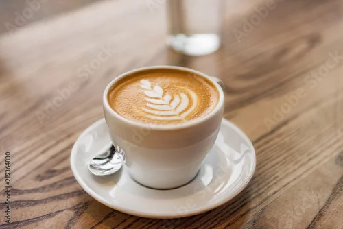 Obraz Latte art in cappuccino coffee cup at cafe table. Closeup of rosetta flower drawing in foam.