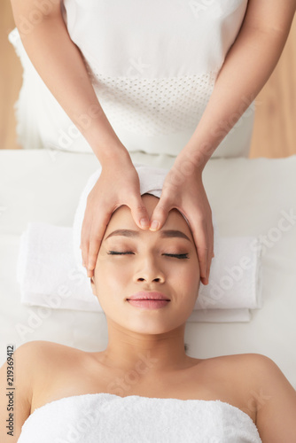 Hands of beautician massaging face of pretty female client