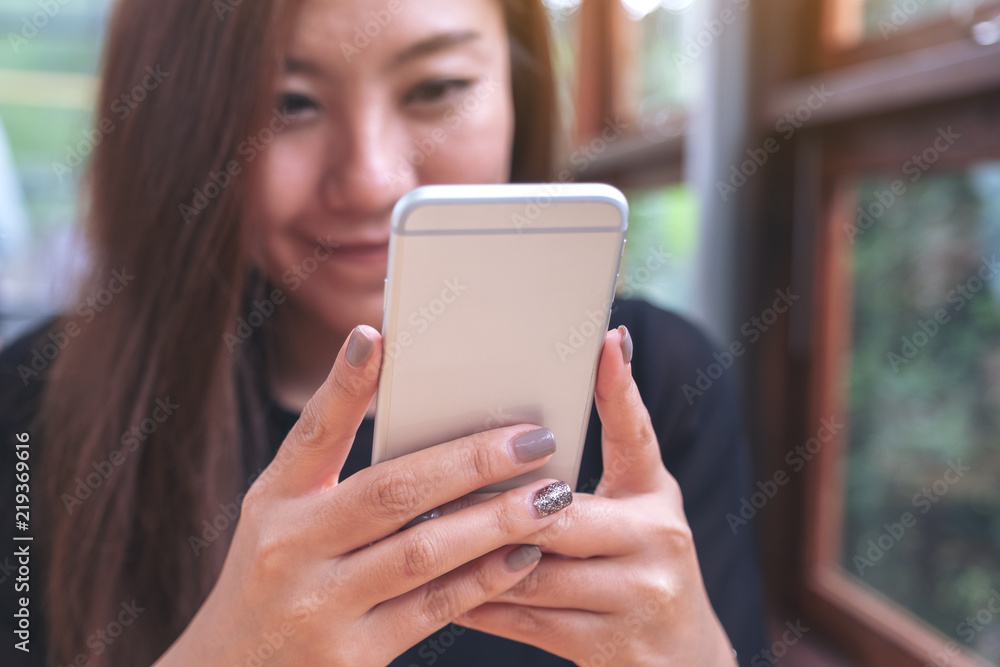 Closeup image of a beautiful Asian woman holding , using and looking at smart phone with feeling happy Closeup image of a beautiful Asian woman holding , using and looking at smart phone with feeling happy