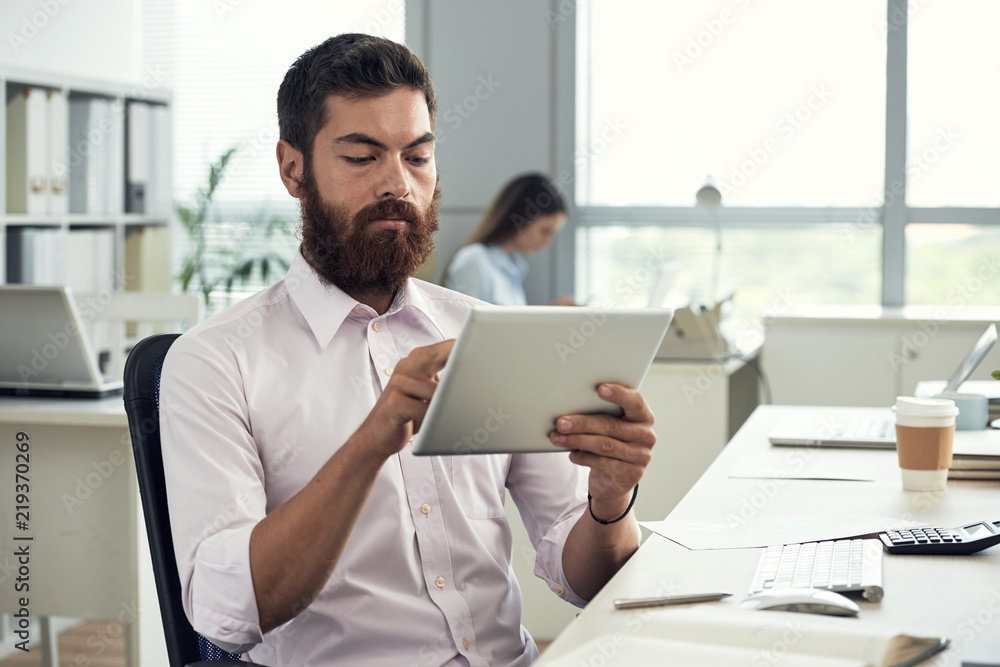 Handsome bearded businessman reading data on digital tablet