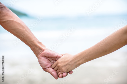 Summer couple holding hands at sunset on beach. Romantic young couple enjoying sun, sunshine, romance and love by the sea. Couple on summer vacation travel holiday. © kanpisut