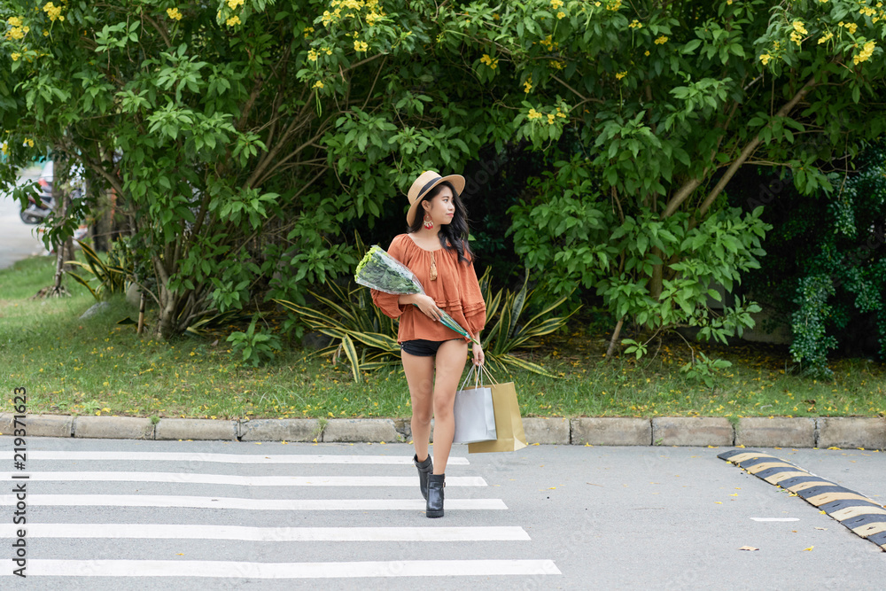 Young stylish woman with flowers at paper-bags crossing road