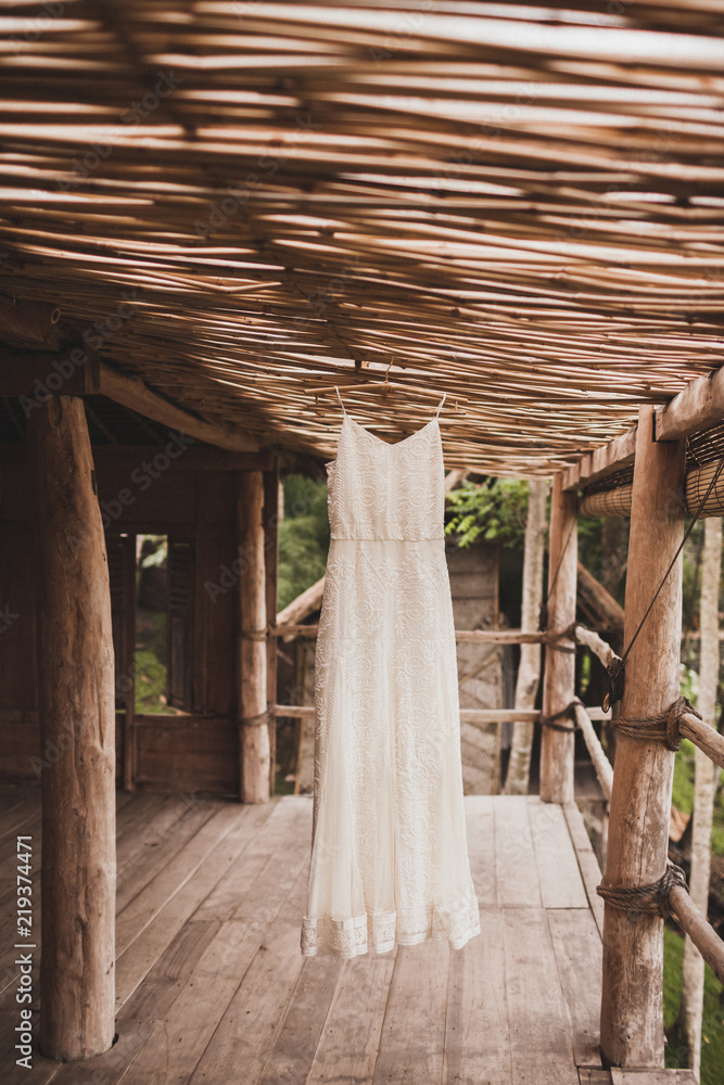 White wedding dress hanging in tropical bamboo house in morning. Bride getting ready White wedding dress hanging in tropical bamboo house in morning. Bride getting ready