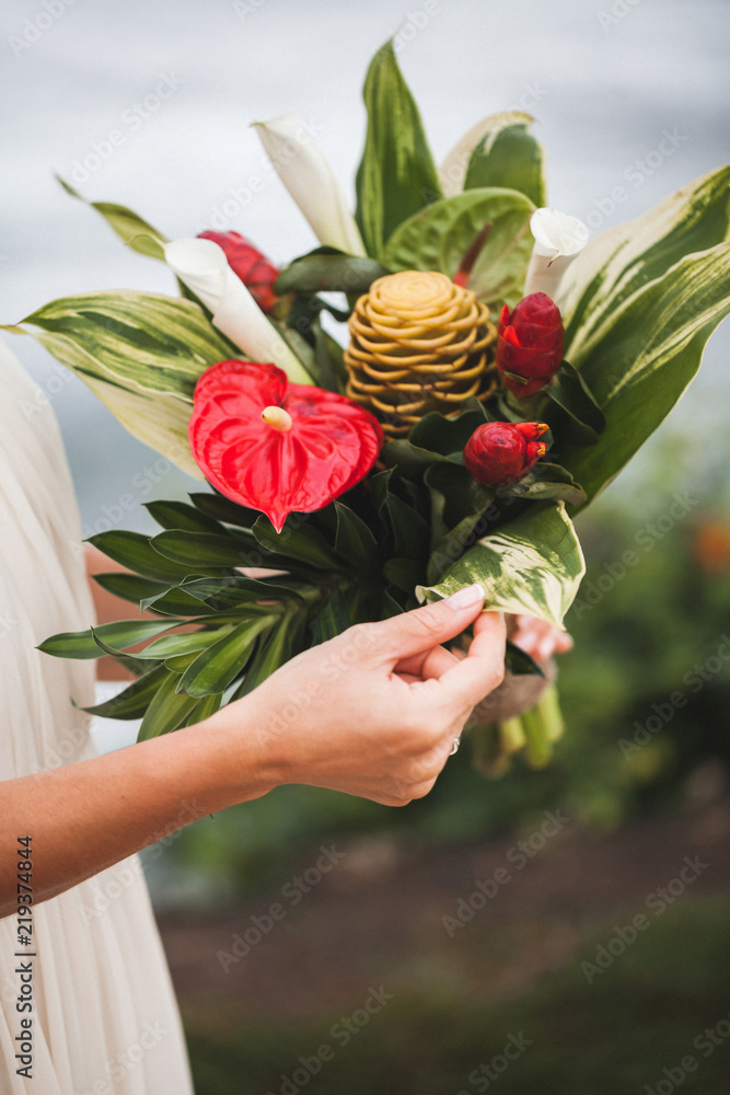 Bouquet with red and green tropical flowers in bride's hands