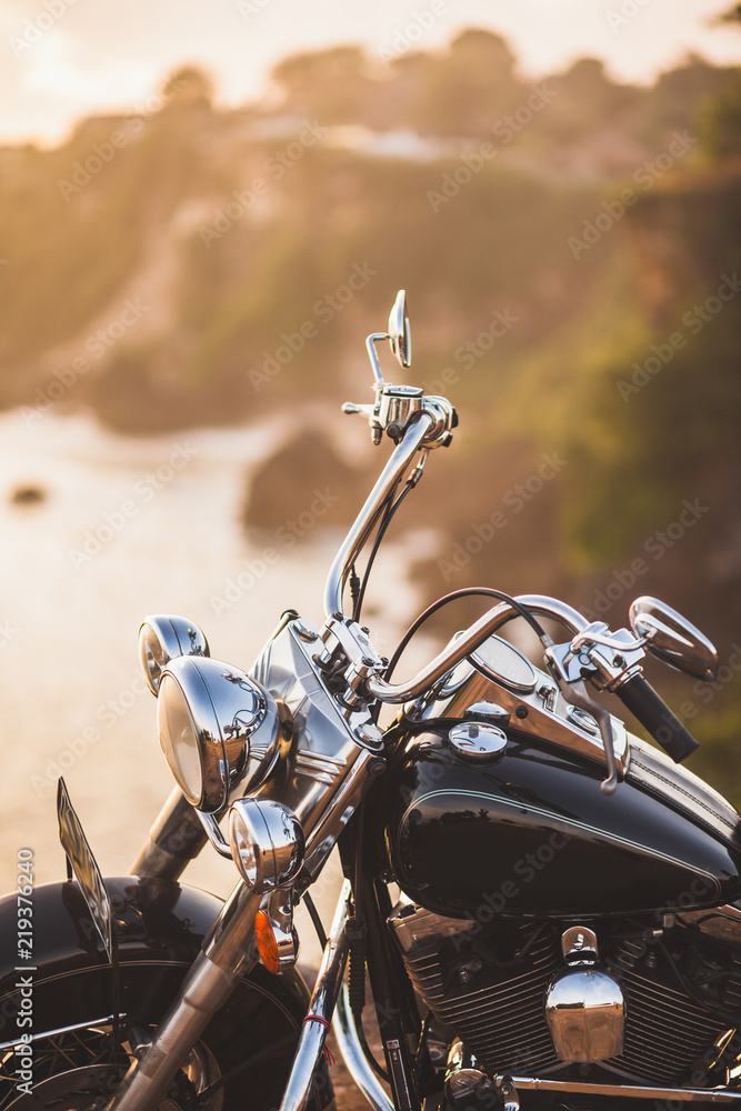 Fototapeta premium Old vintage motorcycle standing on the edge of cliff in warm sunlight at sunrise, shiny details of bike close-up