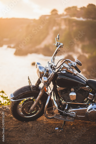 Old vintage motorcycle standing on the edge of cliff in warm sunlight at sunrise, shiny details of bike close-up